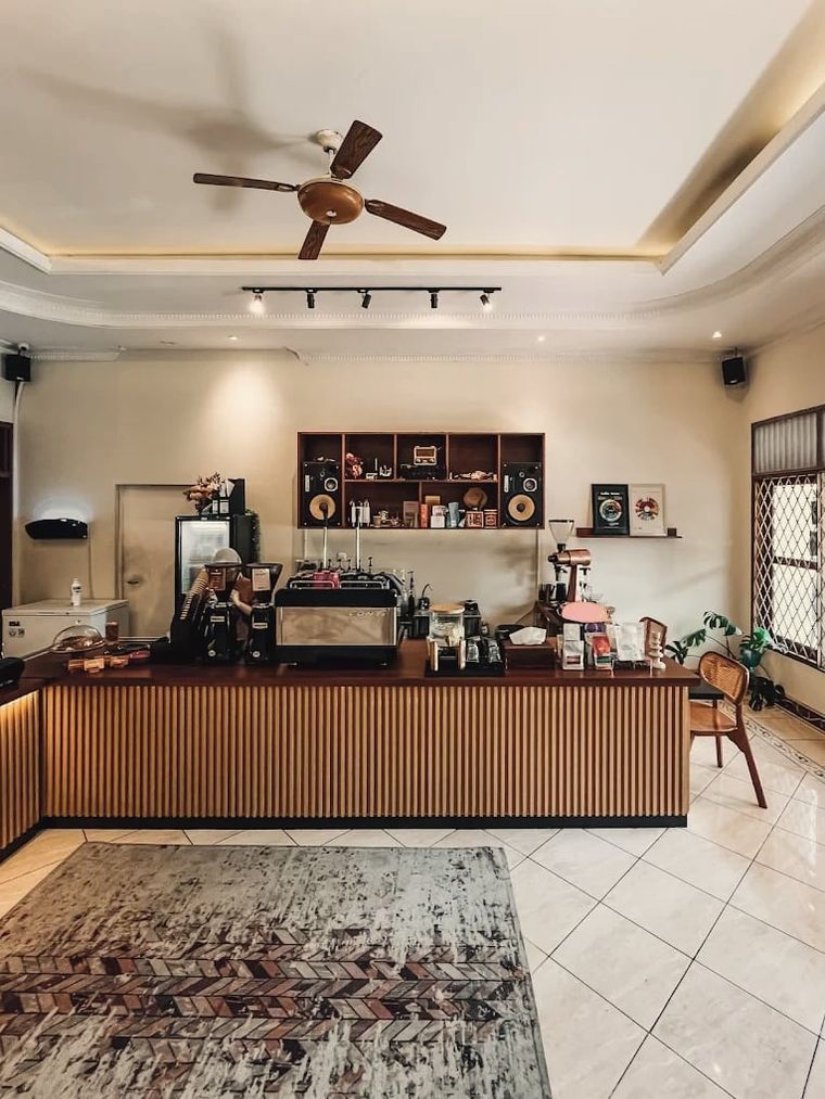 Meja bar berlapis kayu dengan mesin espresso, grinder, dan rak dengan pengeras suara