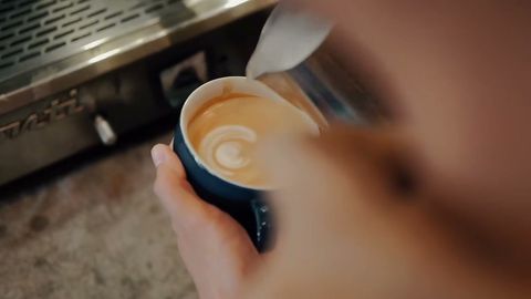 Barista menuang susu membentuk latte art di cangkir biru