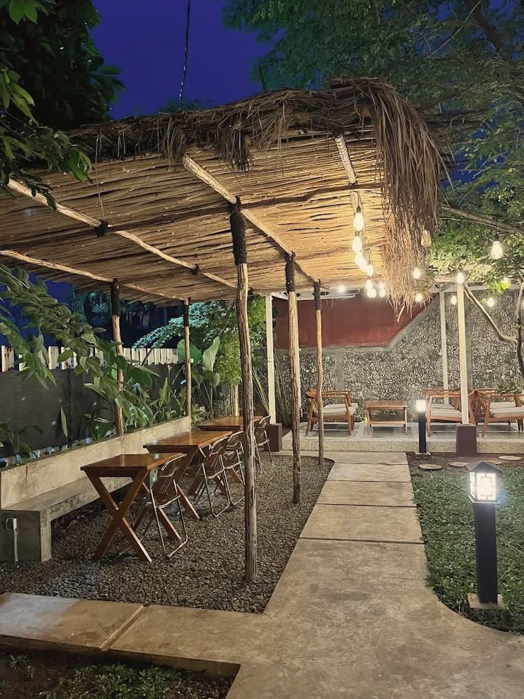 Pergola beratap rumbia pada malam hari dengan meja lipat kayu dan lampu taman