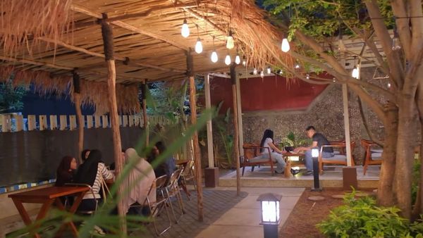 Pergola beratap rumbia dengan lampu bohlam menyala saat senja